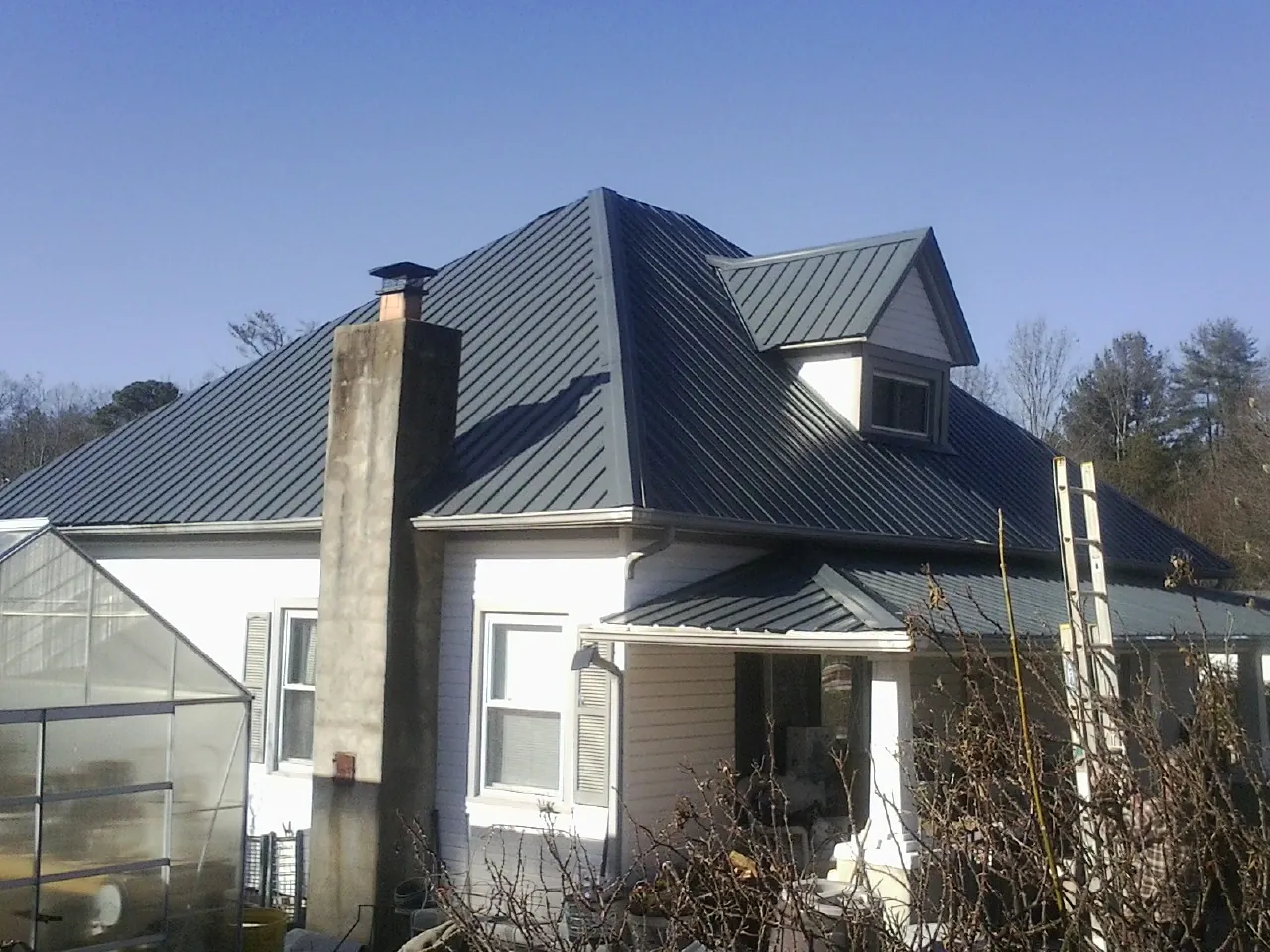 Dark blue standing seam metal roof on a white farmhouse with dormer — Slate & Tile Roof Repair by Roofing Brothers in Red Rock