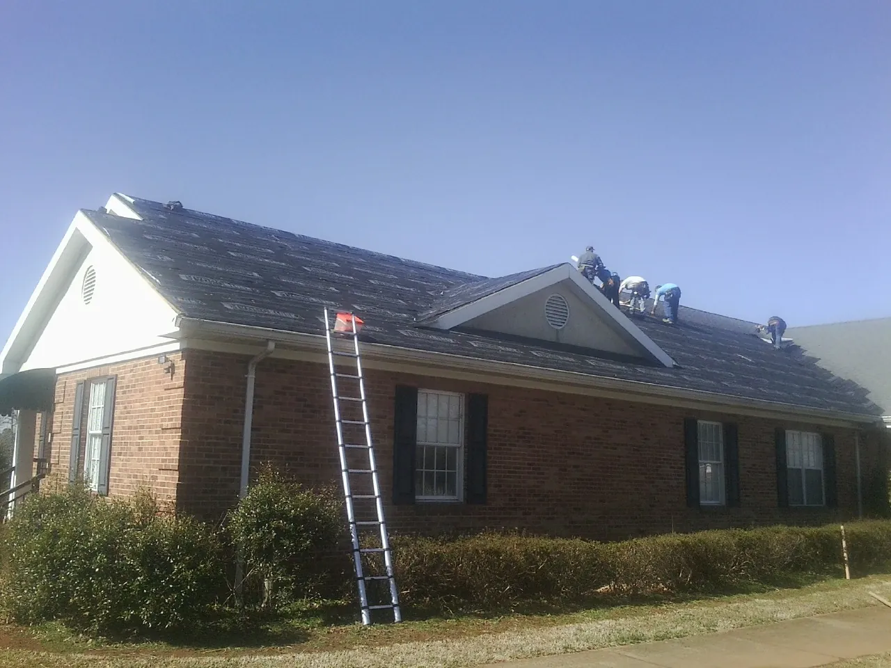 Crew tearing shingles off a brick ranch roof with a ladder set — Metal Roof Repair work by our crew in Red Rock