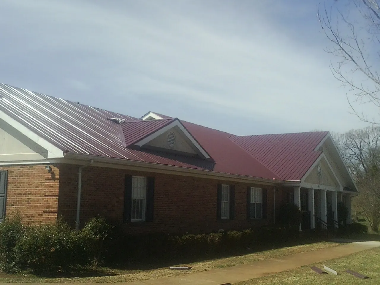 Red metal roof with gabled entries on a long brick building, from a Hail Damage Roof Repair job in Red Rock