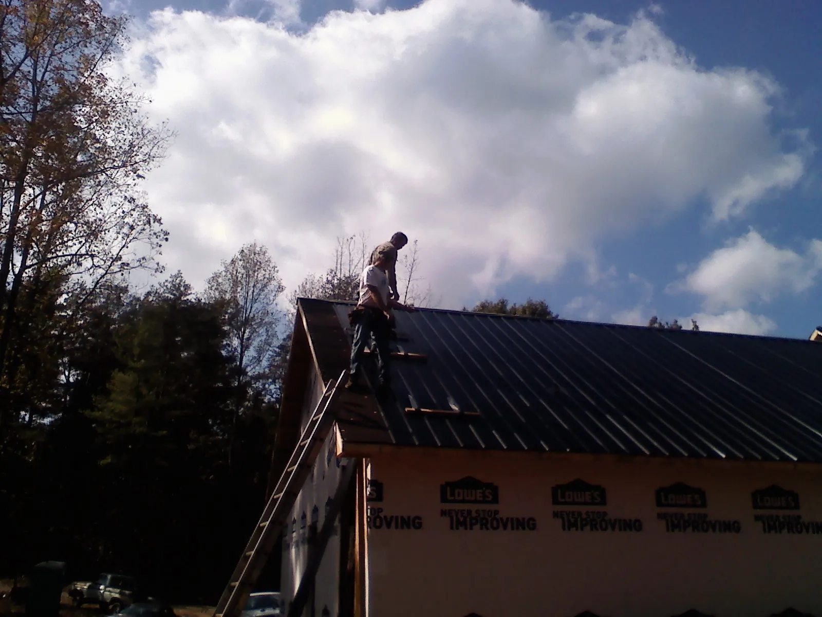 Roofer fastening dark metal panels high against a cloudy sky, from a Roof Inspection job in Red Rock