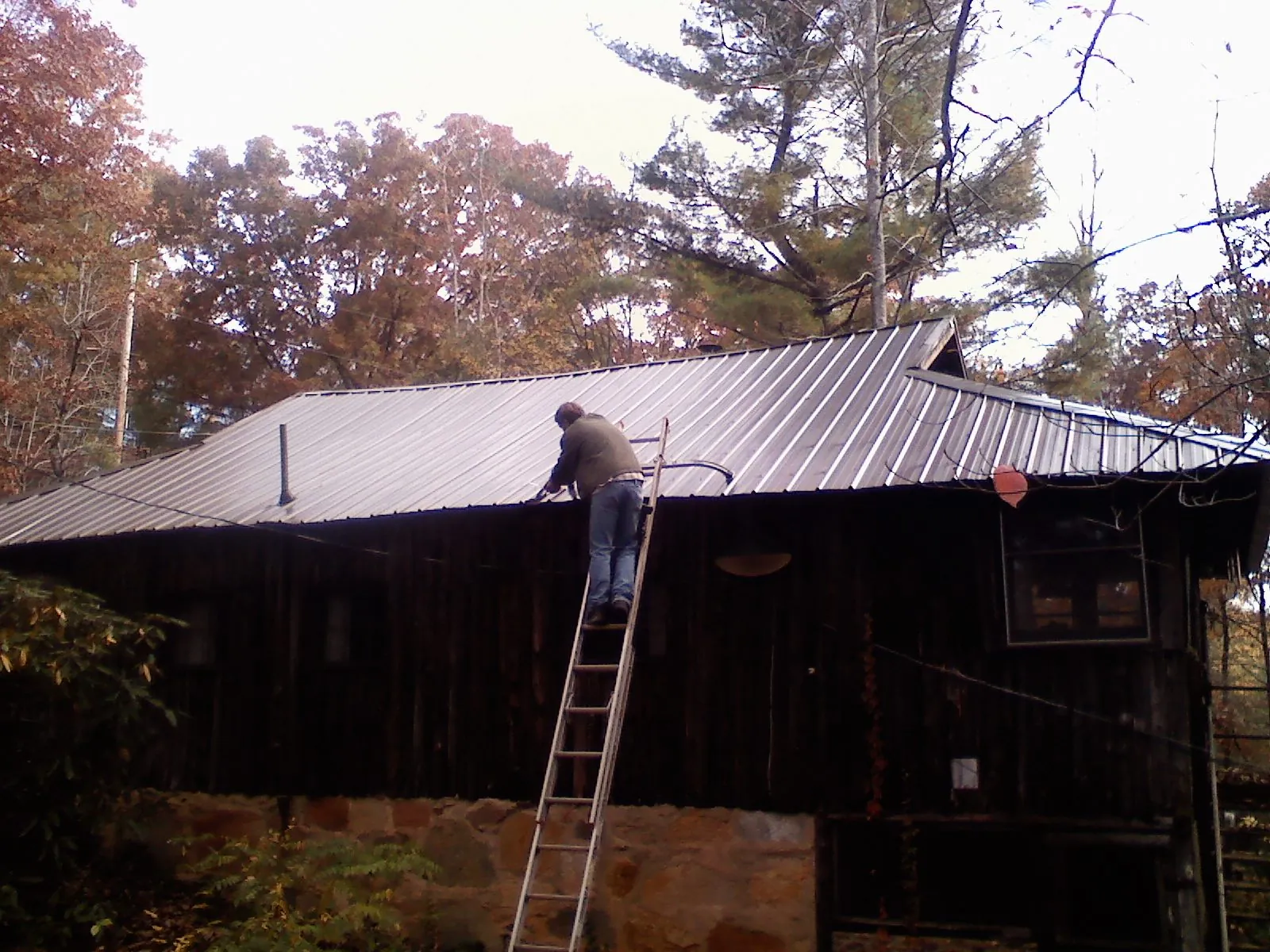 Roofer on a ladder working along the edge of a cabin metal roof in Red Rock